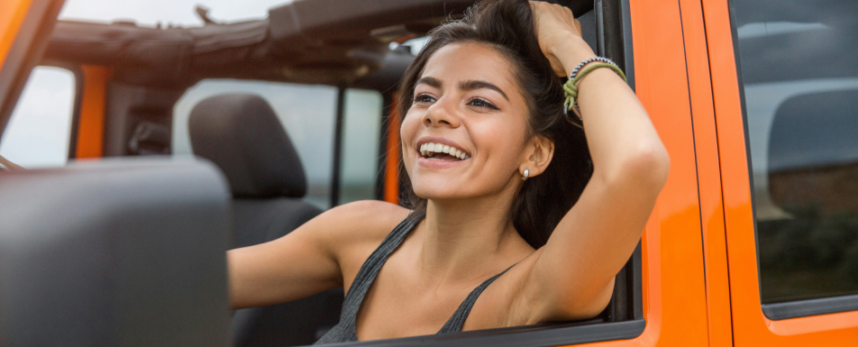 Young woman smiling and driving an orange vehicle.